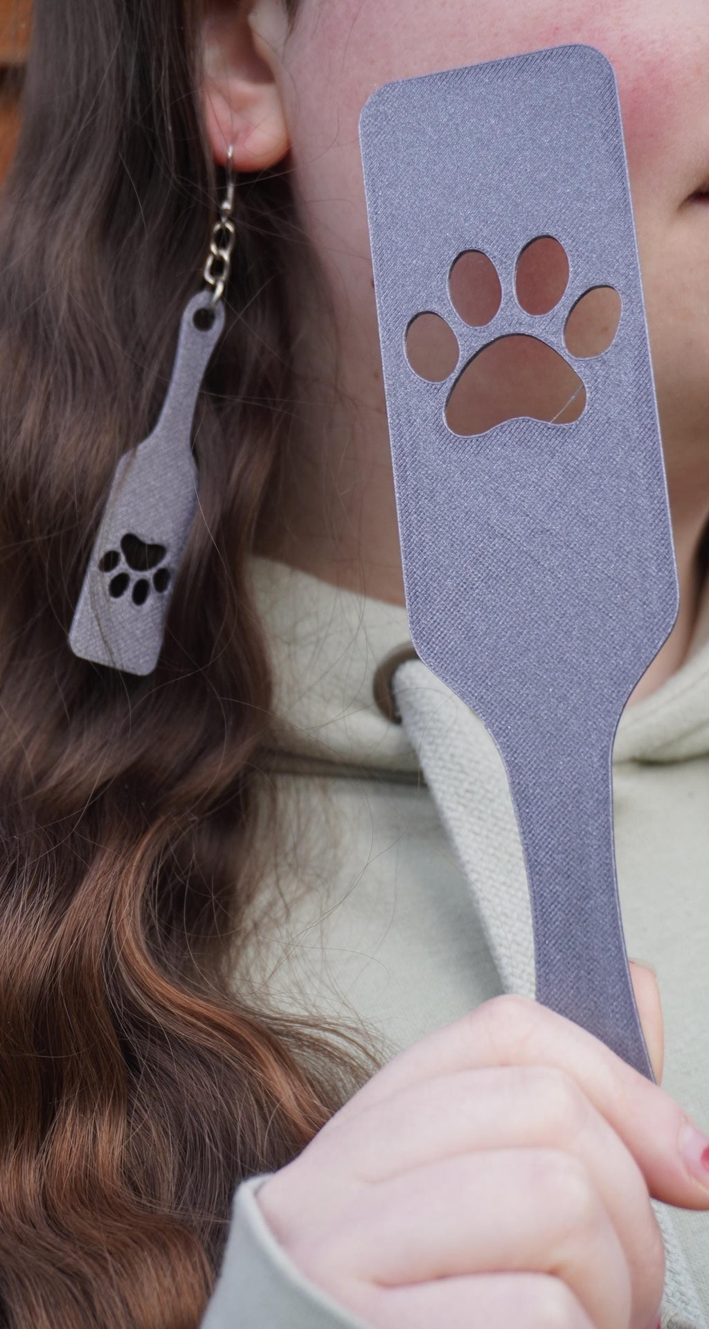 May include: A person wearing a light green hoodie holds a grey plastic spatula with a paw print cutout. The spatula is approximately 30 cm long.