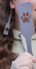 May include: A person wearing a light green hoodie holds a grey plastic spatula with a paw print cutout. The spatula is approximately 30 cm long.