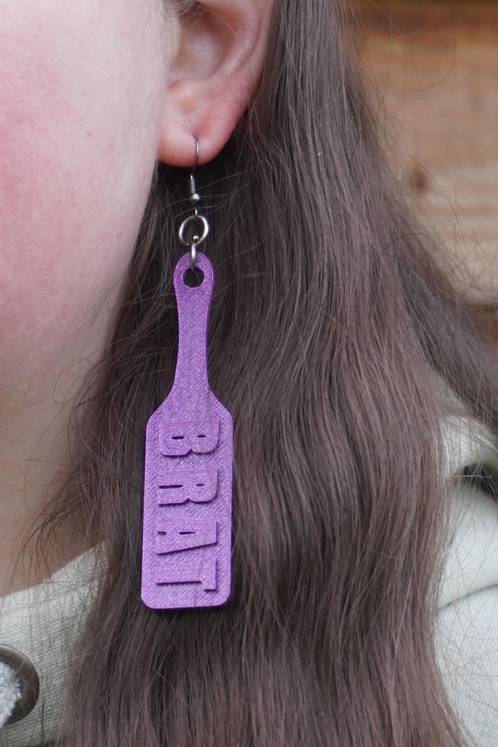 May include: Purple paddle-shaped earrings with the word "BRAT" printed on them. (etsy image id: 7581319508)