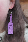 May include: Purple paddle-shaped earrings with the word "BRAT" printed on them. (etsy image id: 7581319508)