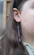 May include: A pair of dangle earrings with a dark grey, textured, elongated pendant. The earrings have a silver hook and two silver rings. (etsy image id: 8005283521)